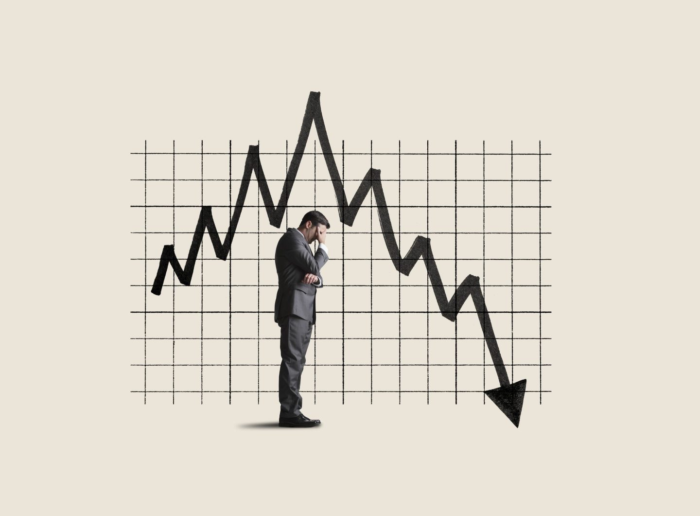 A businessman holds his head in his hands next to a chart showing poor performance.