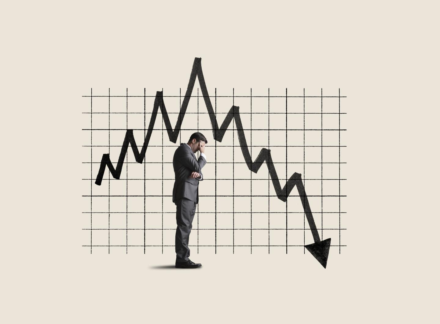 A businessman holds his head in his hands next to a chart showing poor performance.