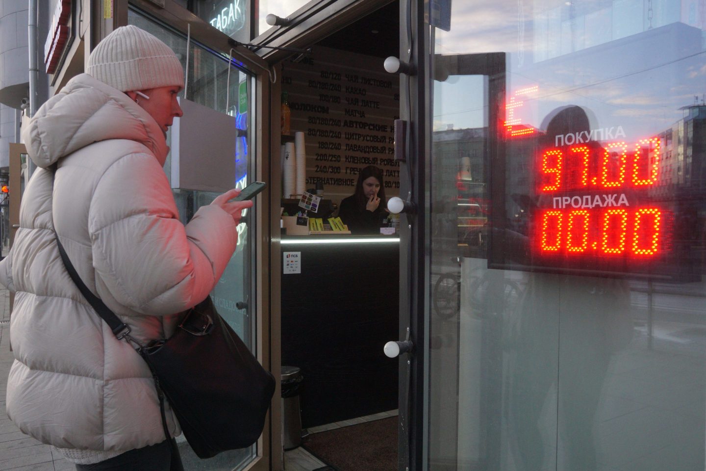 A woman walks into a store with the exchange price of the Russian ruble to U.S. dollar listed next to her.