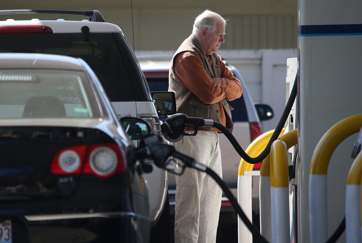 A man stands at a gas pump with arms folded.