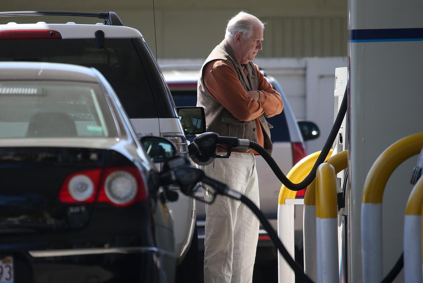 A man stands at a gas pump with arms folded.