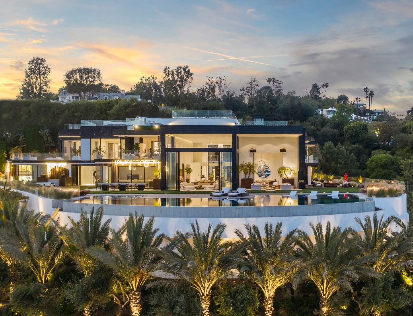 The Bel Air mansion, lit from within, is seen from a distance at sunset.