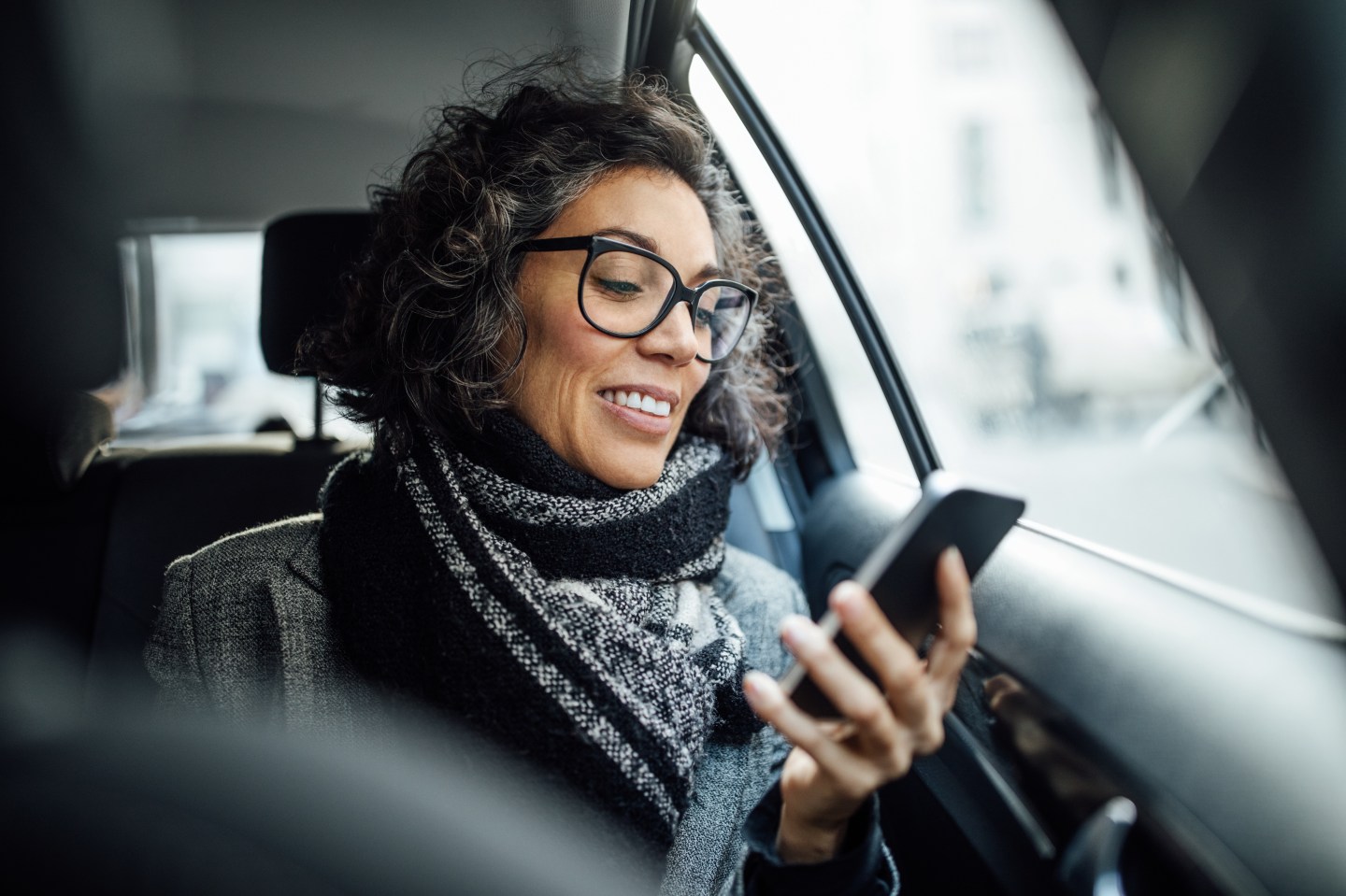 Mature businesswoman reading text message on her cell phone while traveling in a cab.