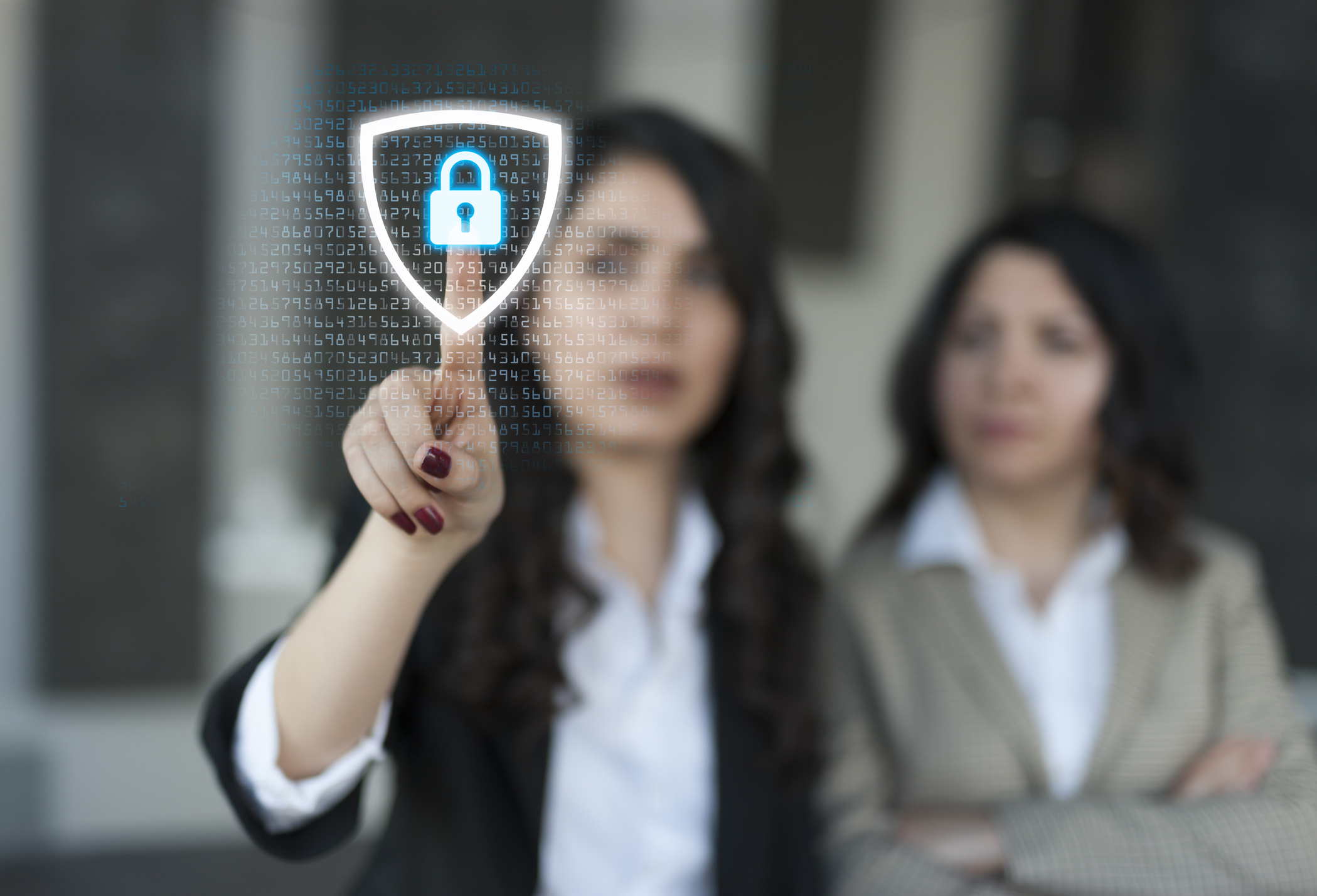 Two women in suits, one tapping a virtual lock symbol