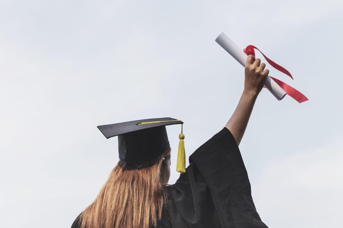 Rear View Of Woman Holding Diploma Against Clear Sky