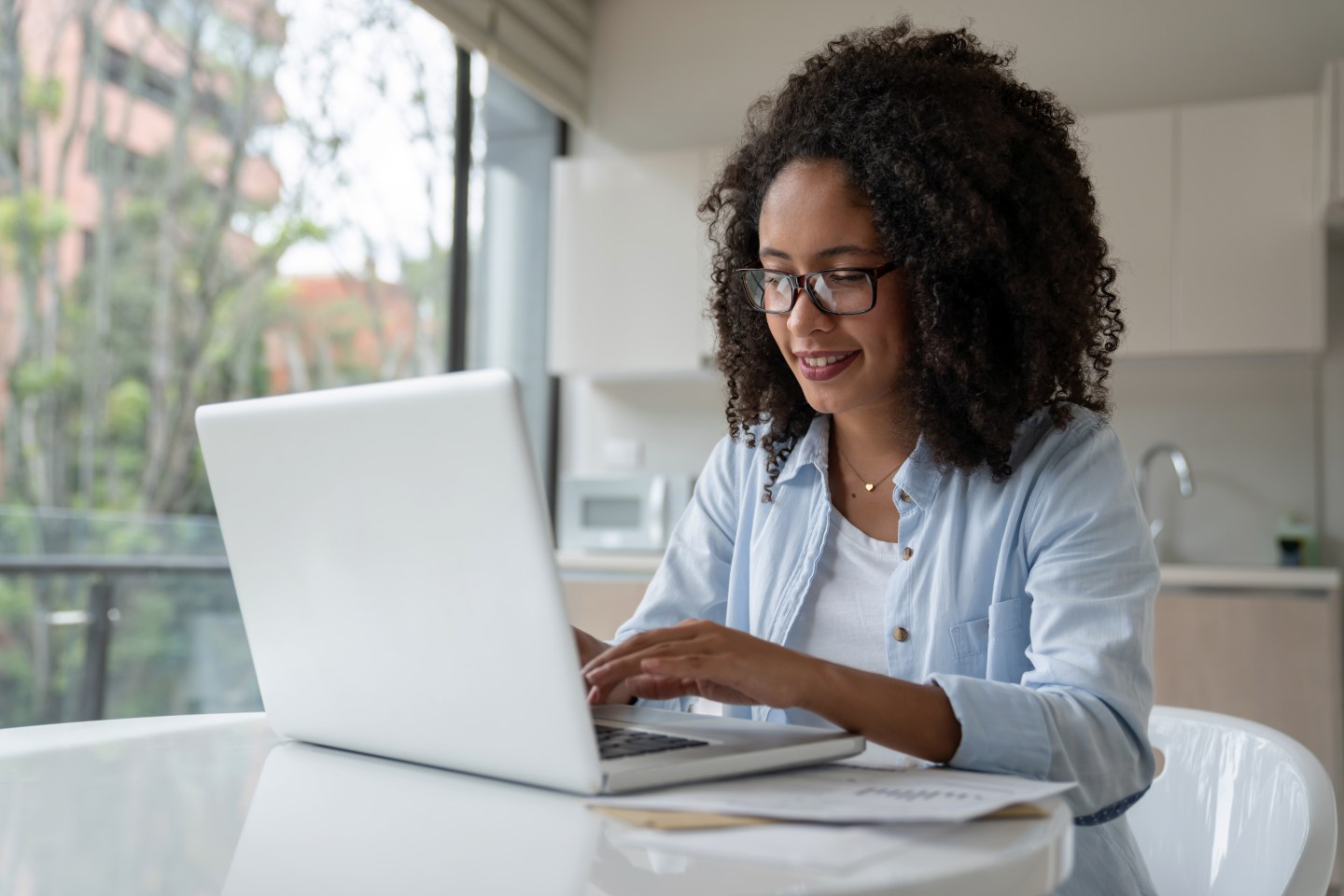 Happy African American woman working online at home using her laptop and wearing glasses - lifestyle concepts