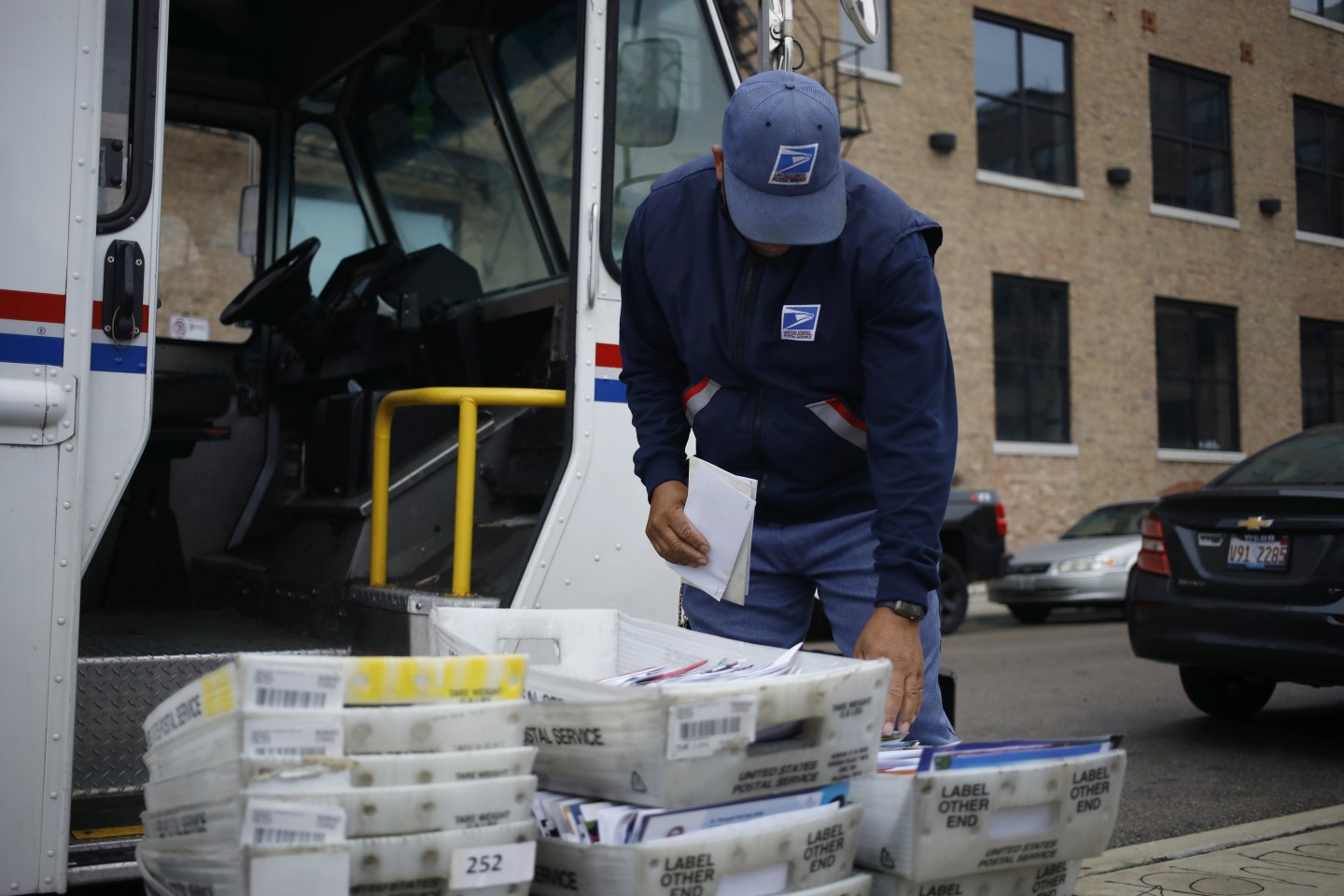 A worker loads mail into a delivery vehicle outside a United States Postal Service.