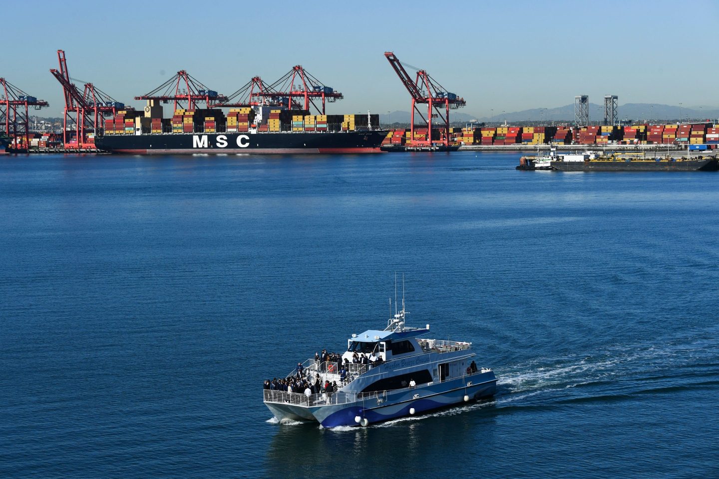 A boat sails past container ships in the Port of Long Beach