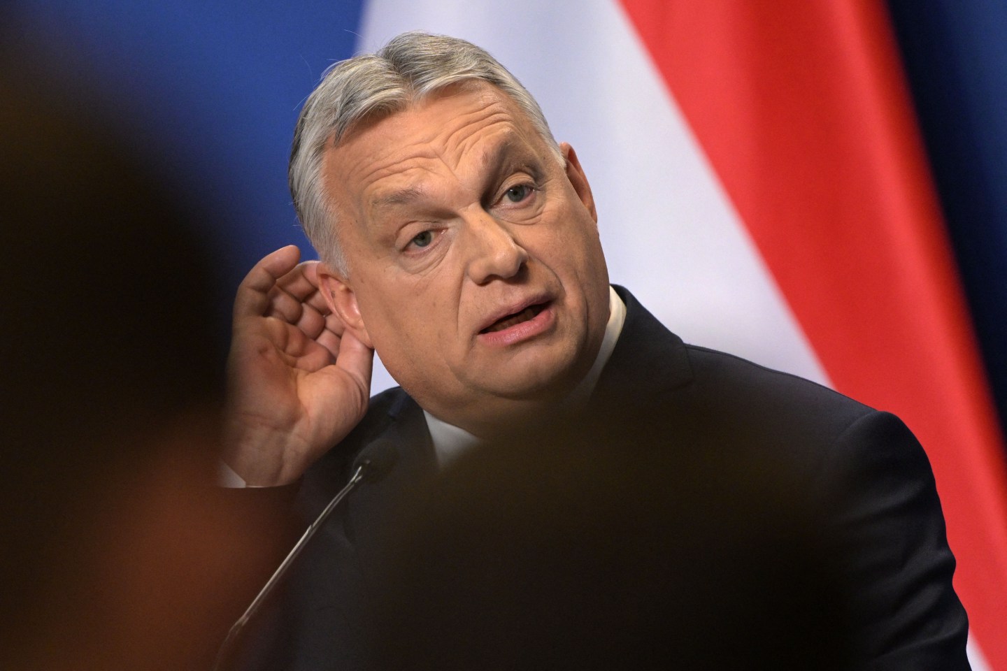 Hungarian Prime Minister Viktor Orbán is seen speaking into a microphone onstage at a press briefing.