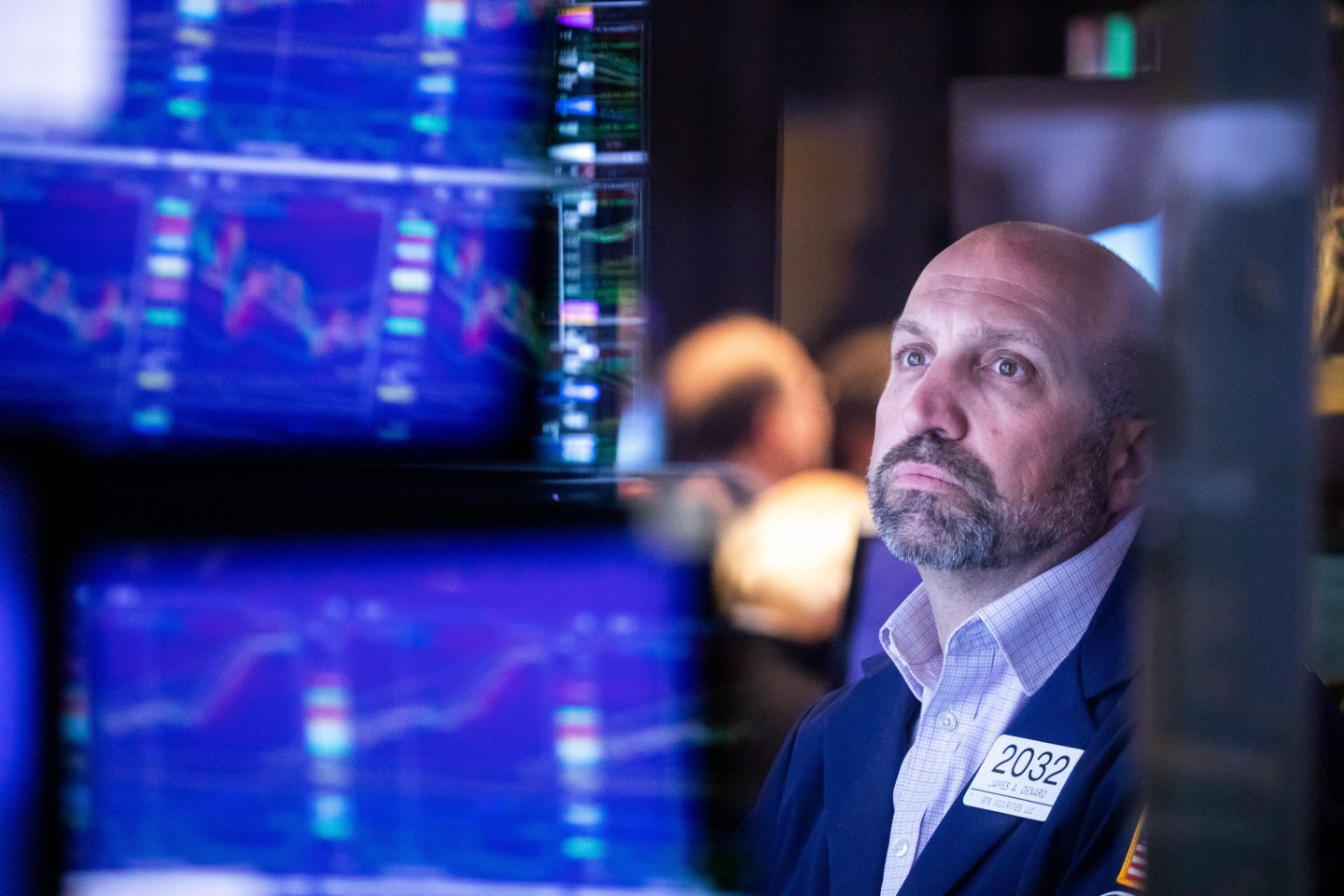 A trader at the New York Stock Exchange is seen among screens displaying various charts.