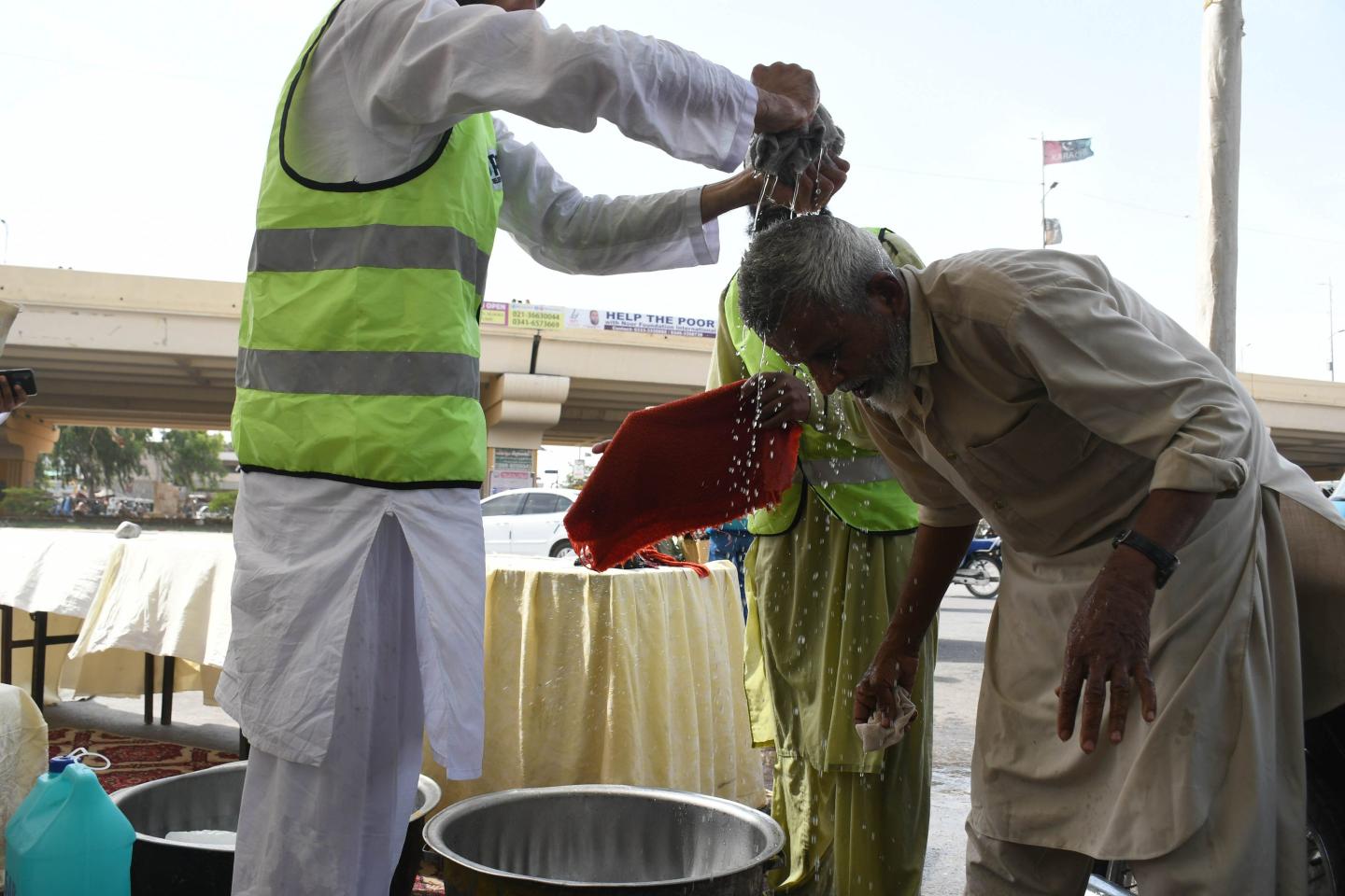 A volunteer squeezes water from a wet towel over an older man's head during a heatwave in Pakistan