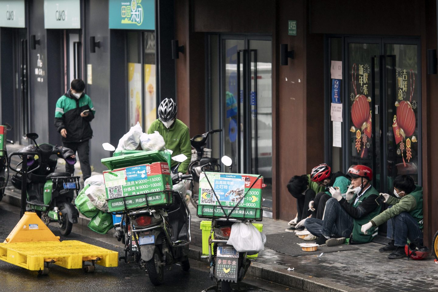 Chinese delivery drivers sit by their motorcycles during Shanghai's lockdown