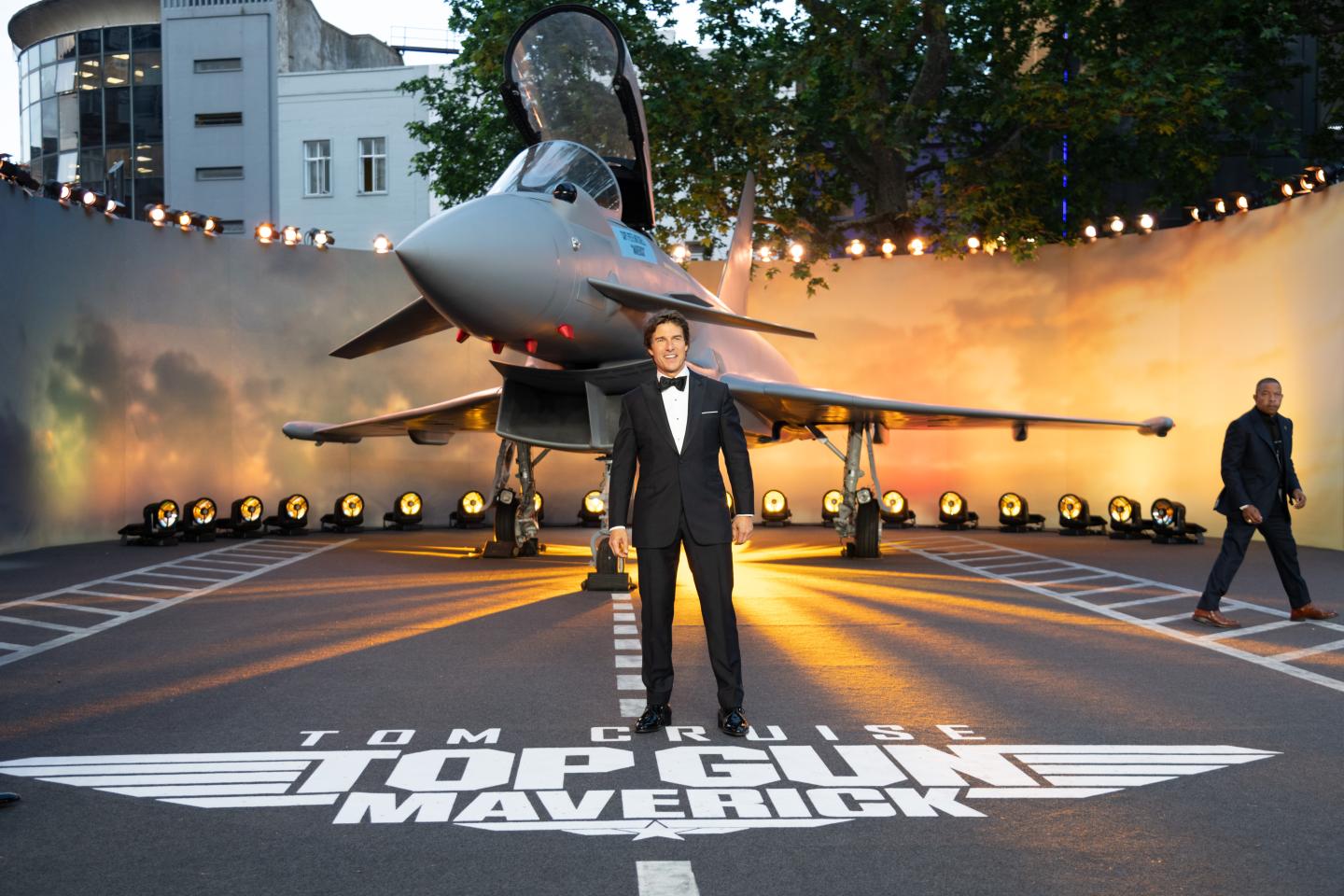 Tom Cruise stands in front of a fighter jet at a film premiere.