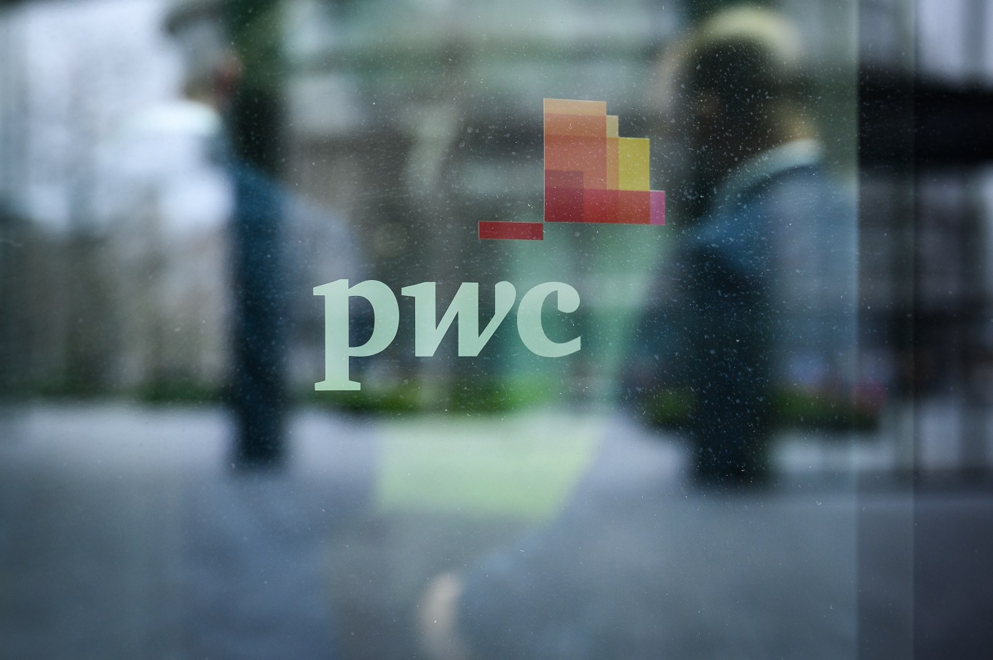 People walk past a sign on a window on the exterior of the PWC