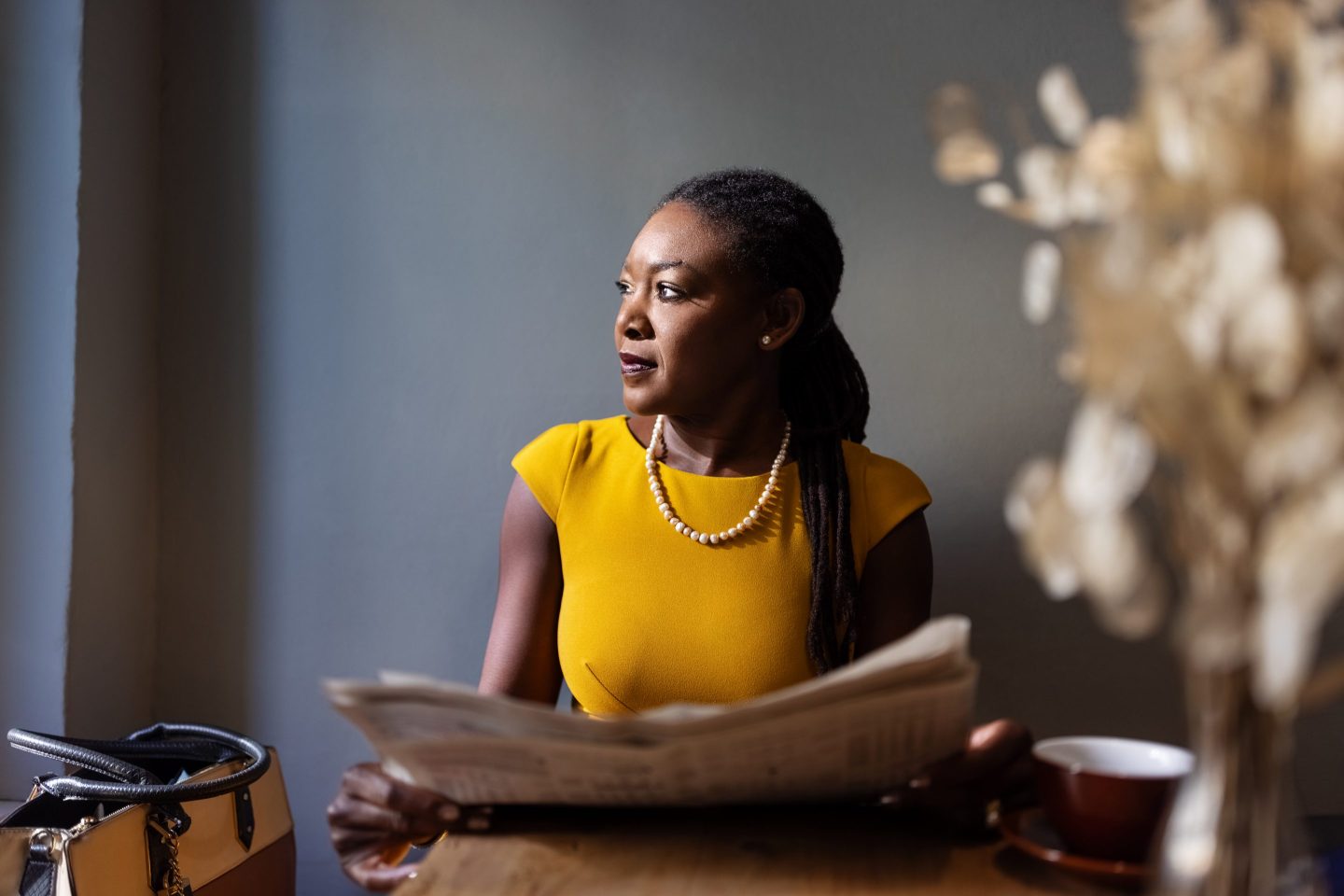 Black woman with newspaper sitting at cafe looking away