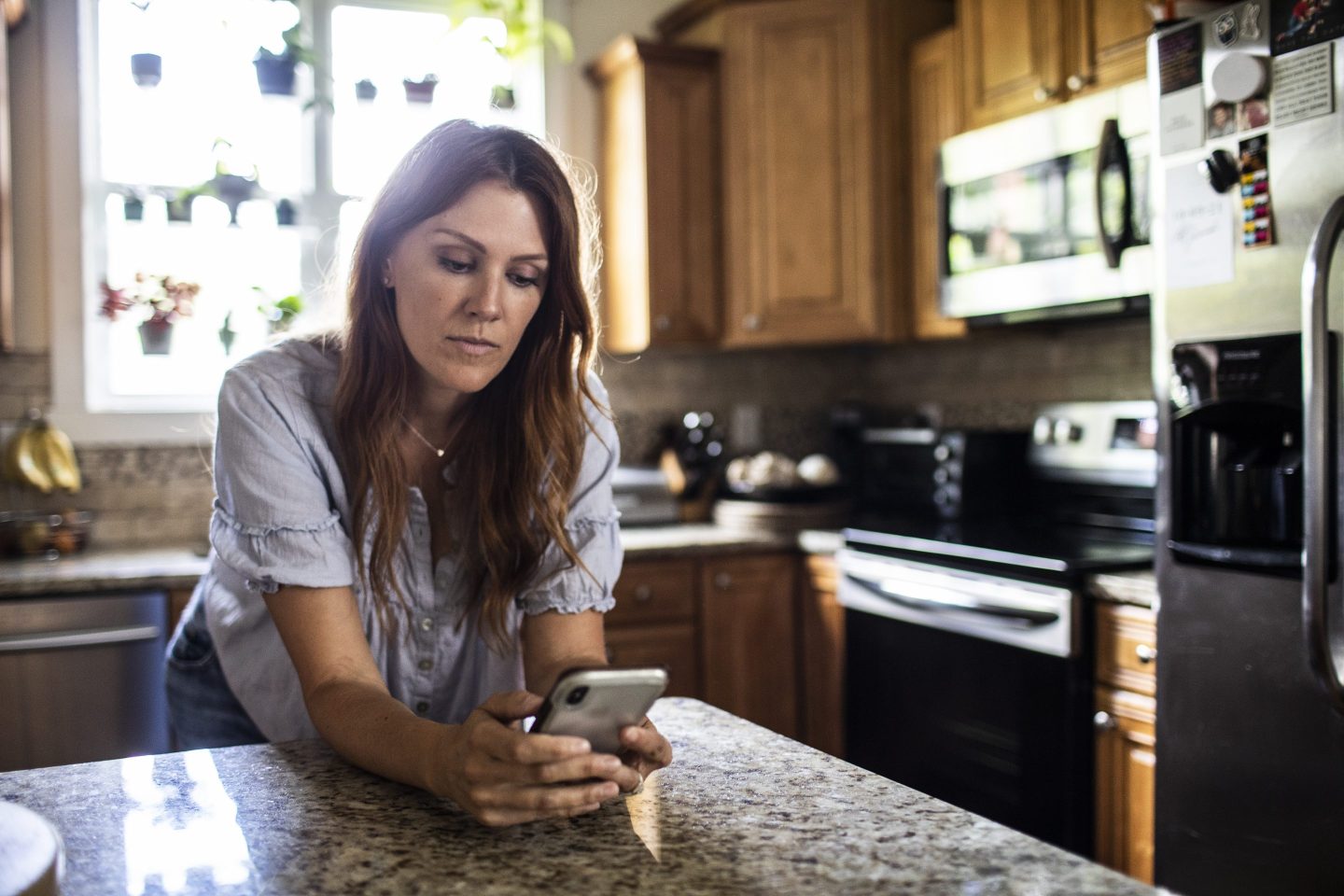 Woman using mobile device in kitchen at home
