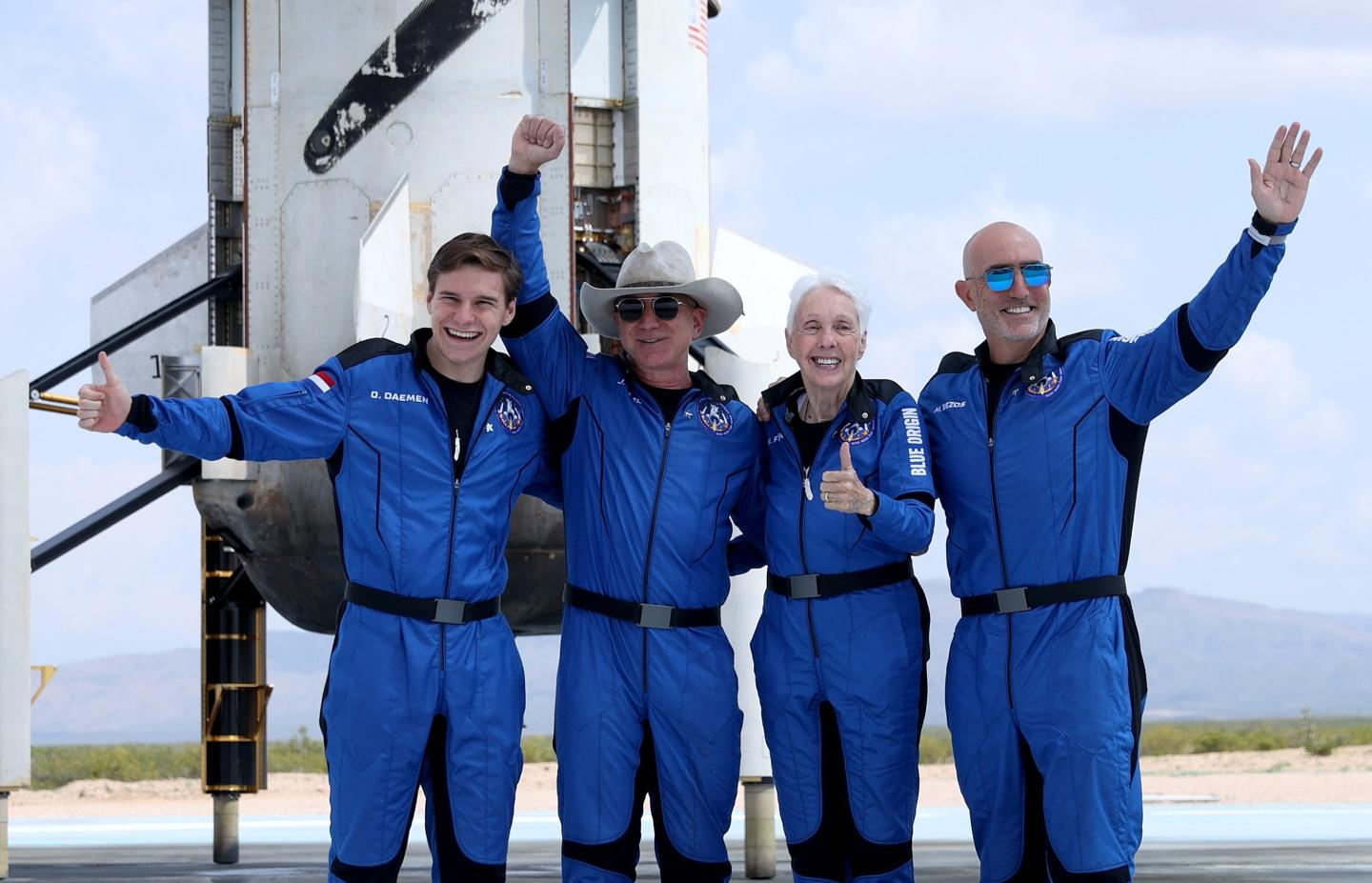 Jeff Bezos and the other passengers pose in front o the Blue Origin rocket.