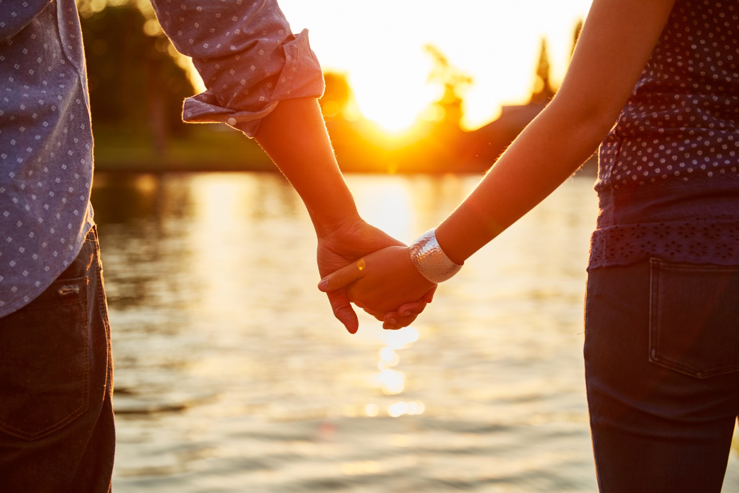 A couple is seen holding hands next to a river.