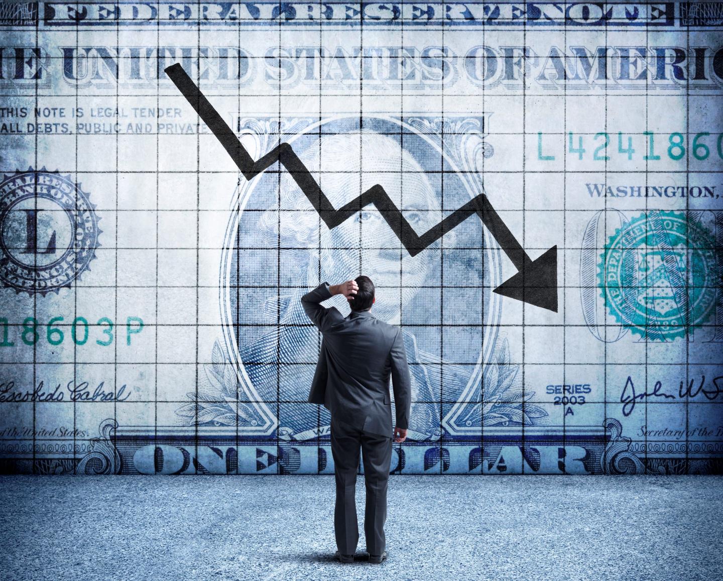 A business man looks at a chart of the U.S. dollar with a downward arrow.