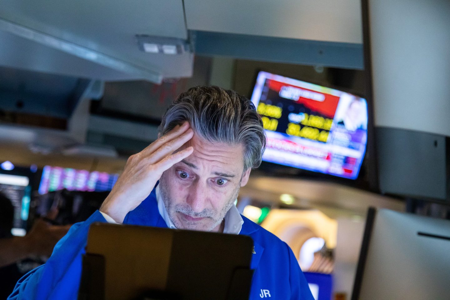 A NYSE trader rubs his head while looking at a computer.