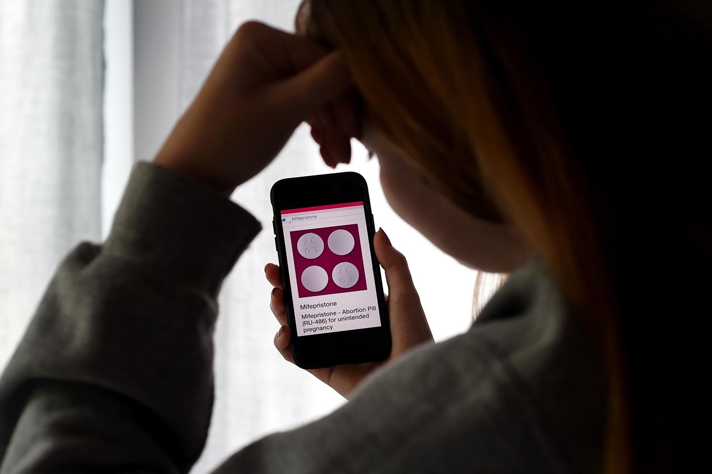 Girl looks at an Abortion Pill (RU-486) for unintended pregnancy from Mifepristone displayed on a smartphone.