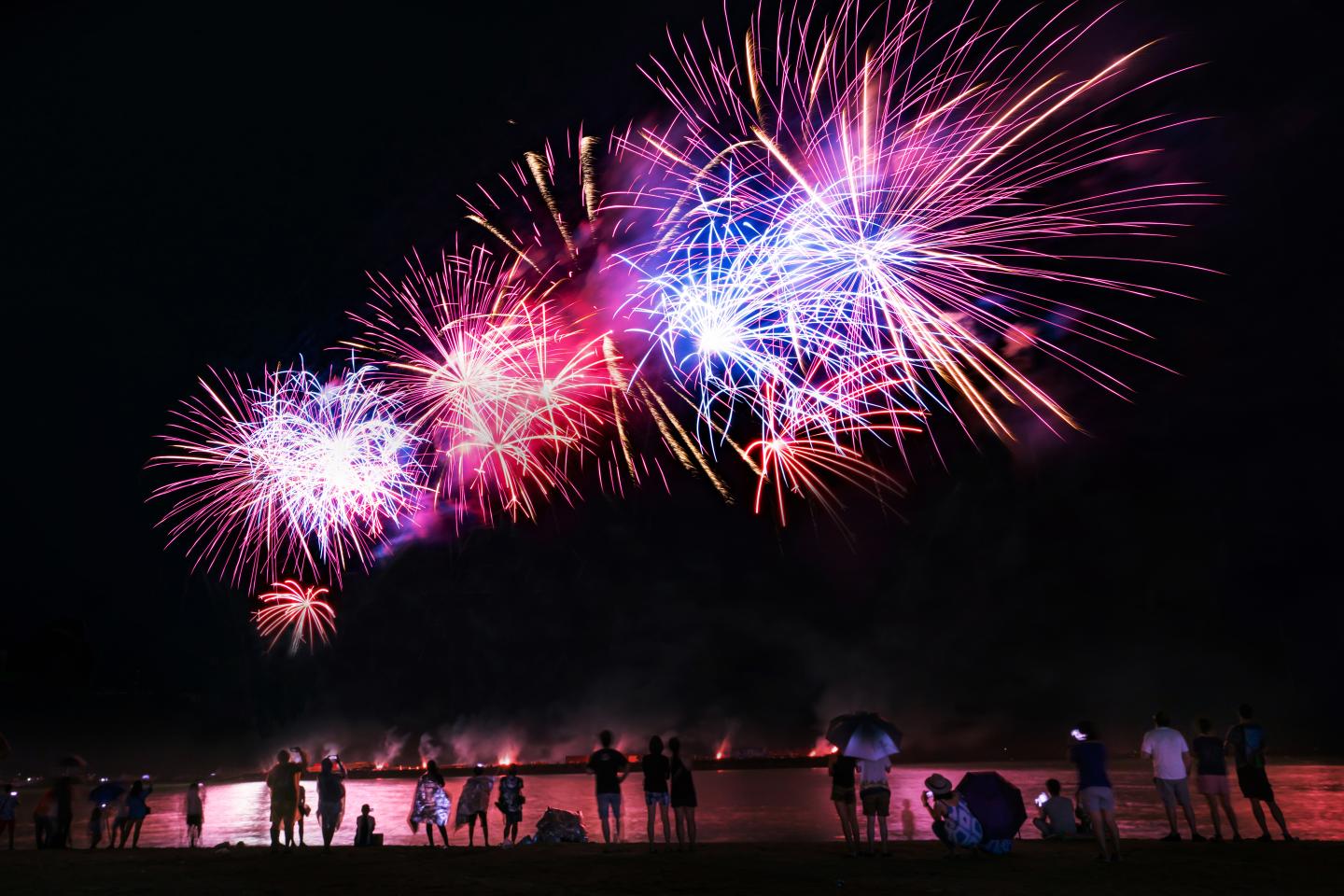 Crowd watching fireworks and celebrating on the beach.