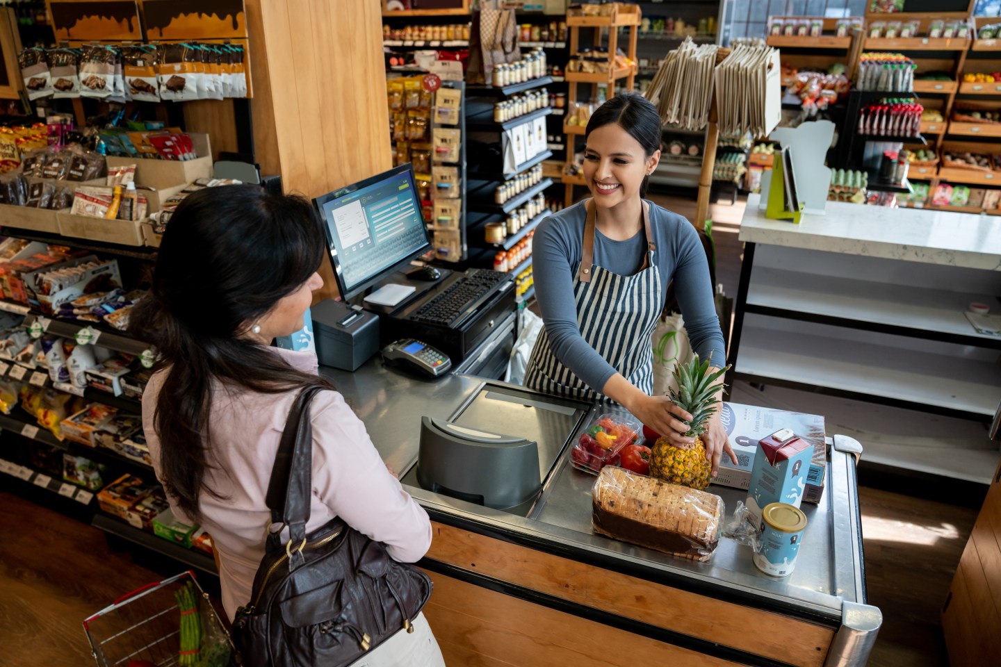 Friendly latin american cashier helping female customer check out passing the products through the bar code reader both smiling