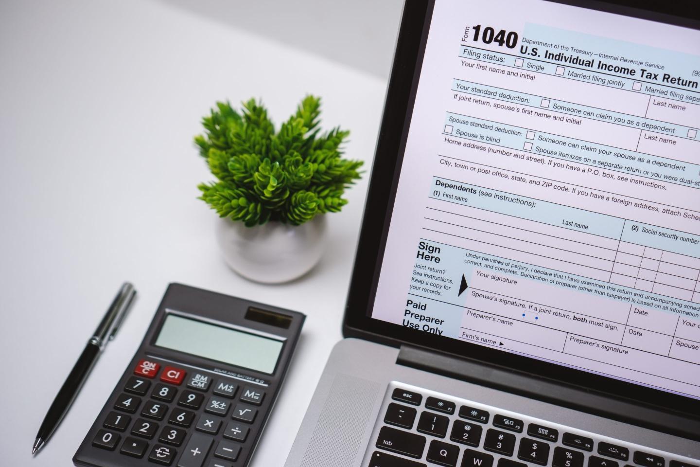 Tax Form on Laptop Screen on Work Desk with Pen and Calculator