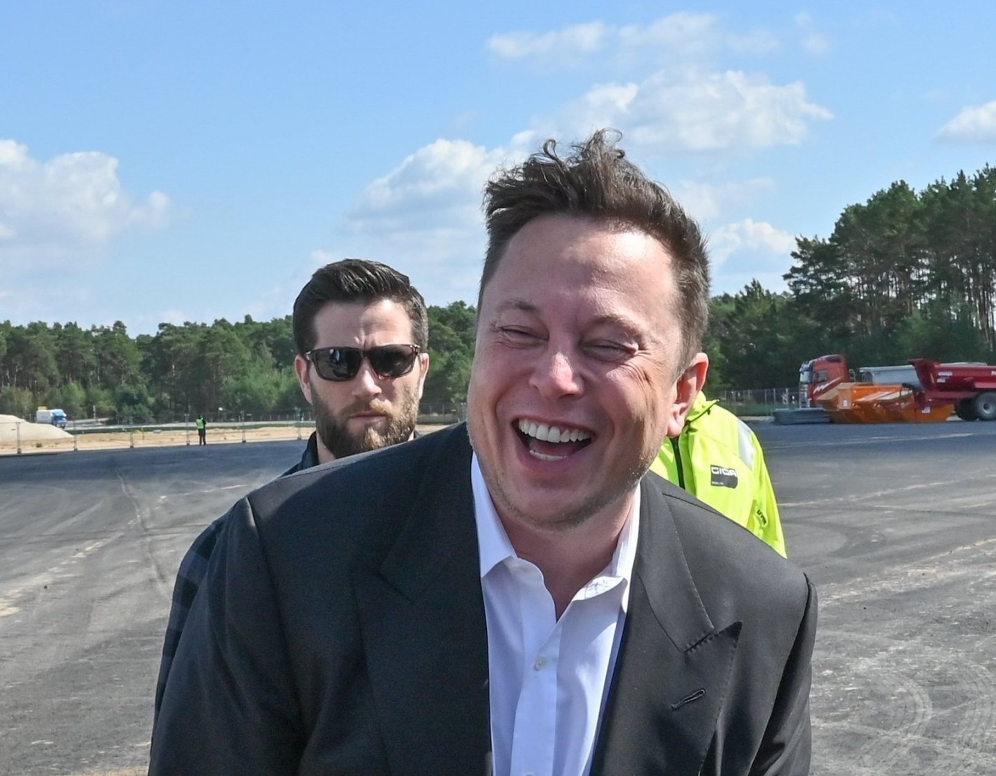 Elon Musk, head of Tesla, stands laughing next to journalists at the Tesla Gigafactory construction site. In Grünheide near Berlin.