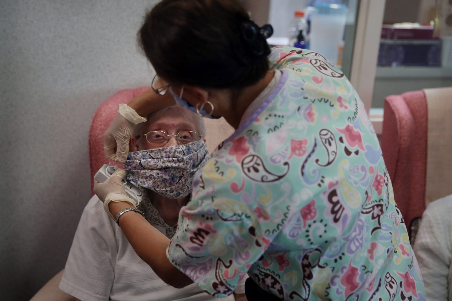 Nurse aid helps elderly woman with mask