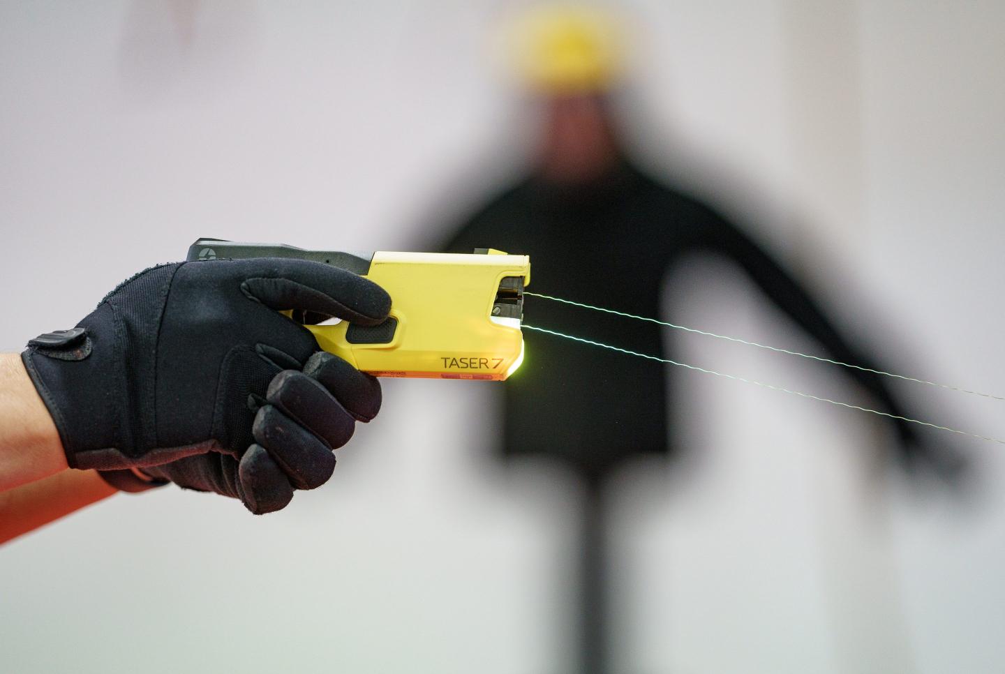 A close up of a gloved police officer firing a yellow taser gun