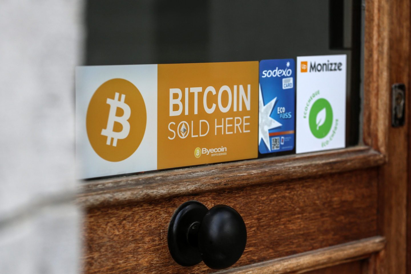 A sign indicating 'Bitcoin Sold Here' in the window of a phone repair store in Antwerp