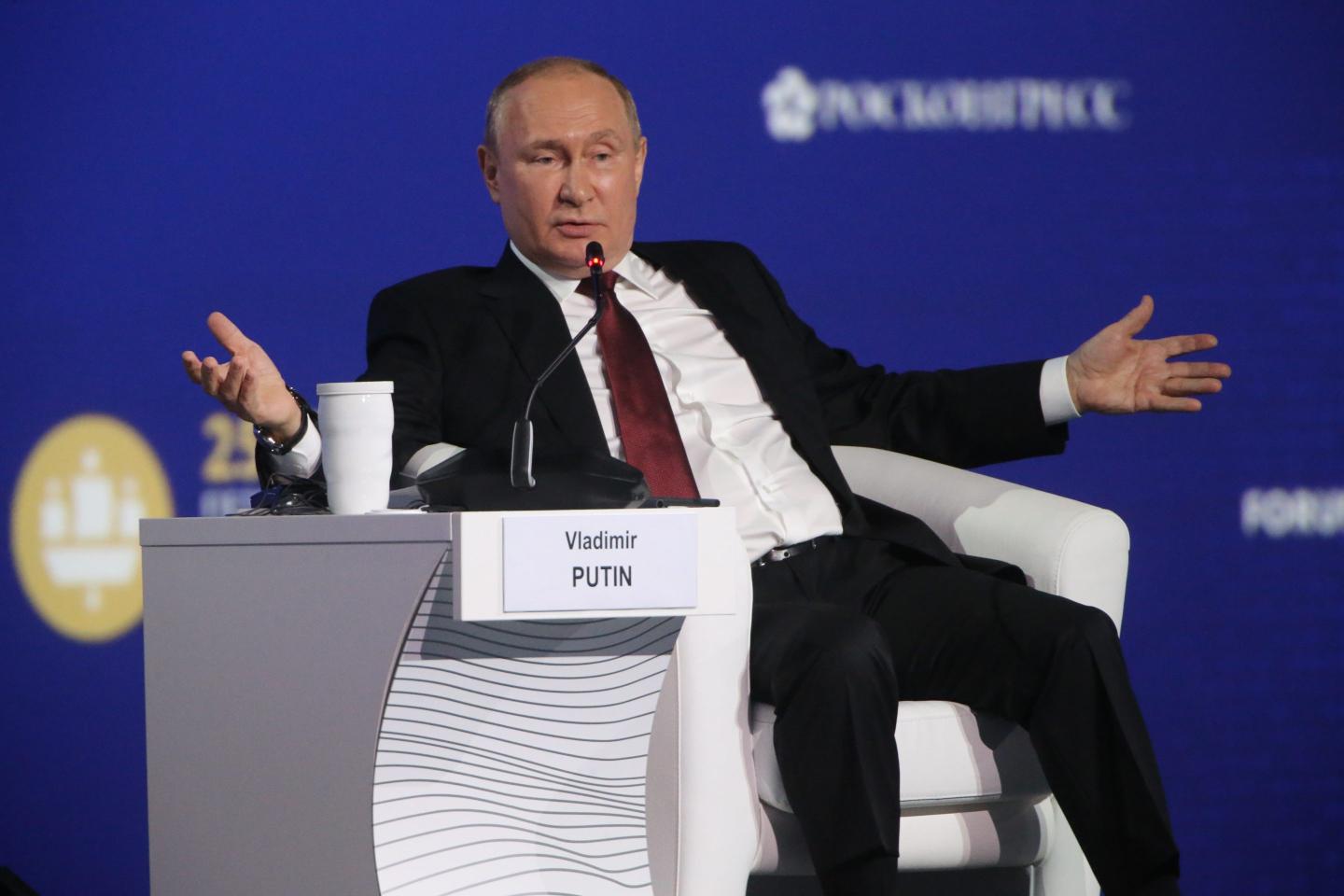 Russia President Vladimir Putin gestures with wide arms while seated on stage at Russia's annual economic forum