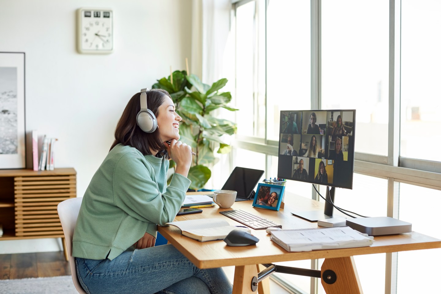 A woman sits at a desk at home while looking at her colleagues on a computer screen during a virtual meeting.