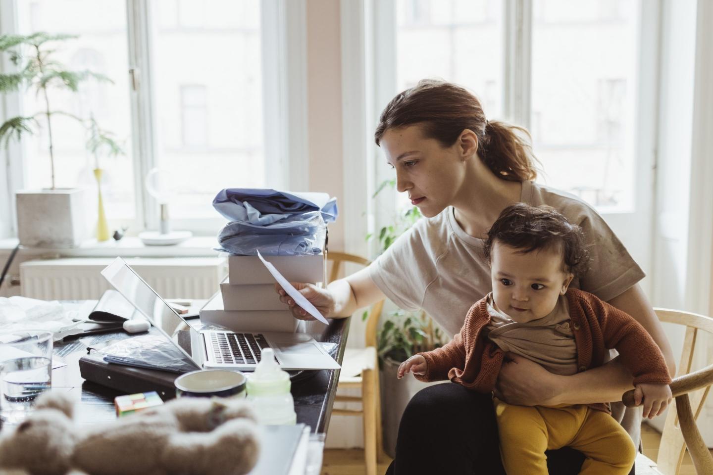 Businesswoman reading document while sitting with baby boy in living room