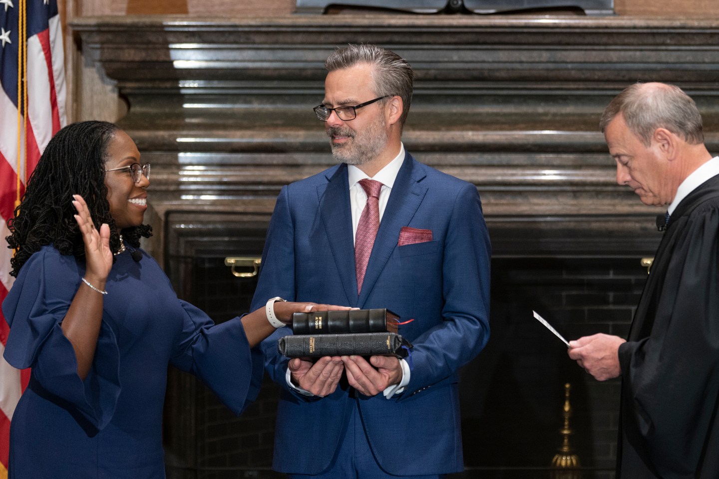 Judge Ketanji Brown Jackson being sworn in by Chief Justice John Roberts, as her husband stands between them.