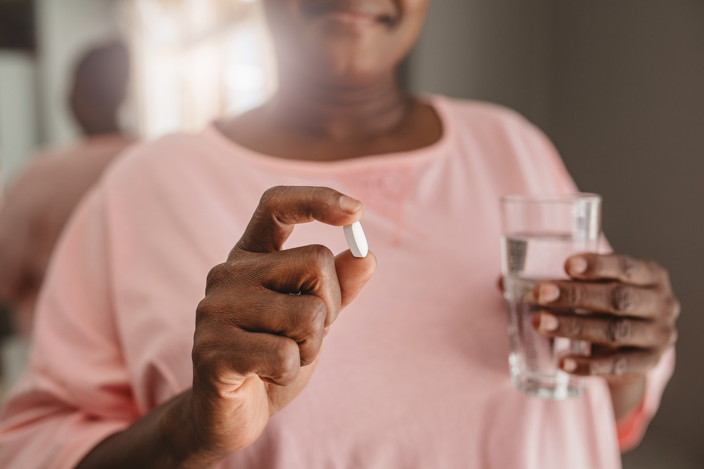 Closeup of an African American woman standing in her bathroom in the morning taking a vitamin with a glass of water.