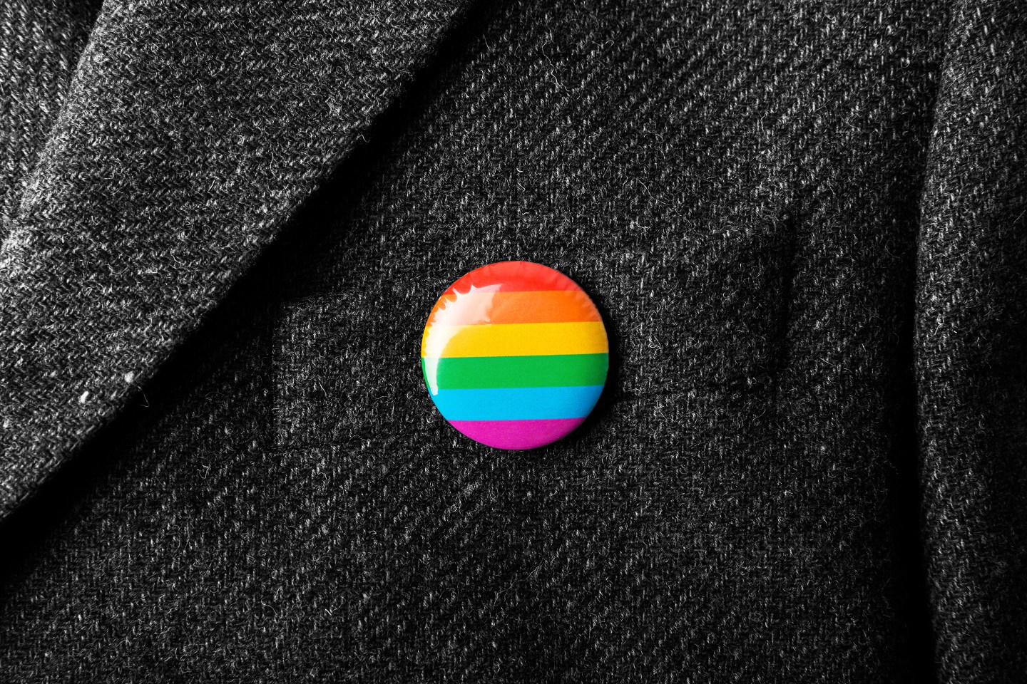 A rainbow lapel pin on a suit jacket