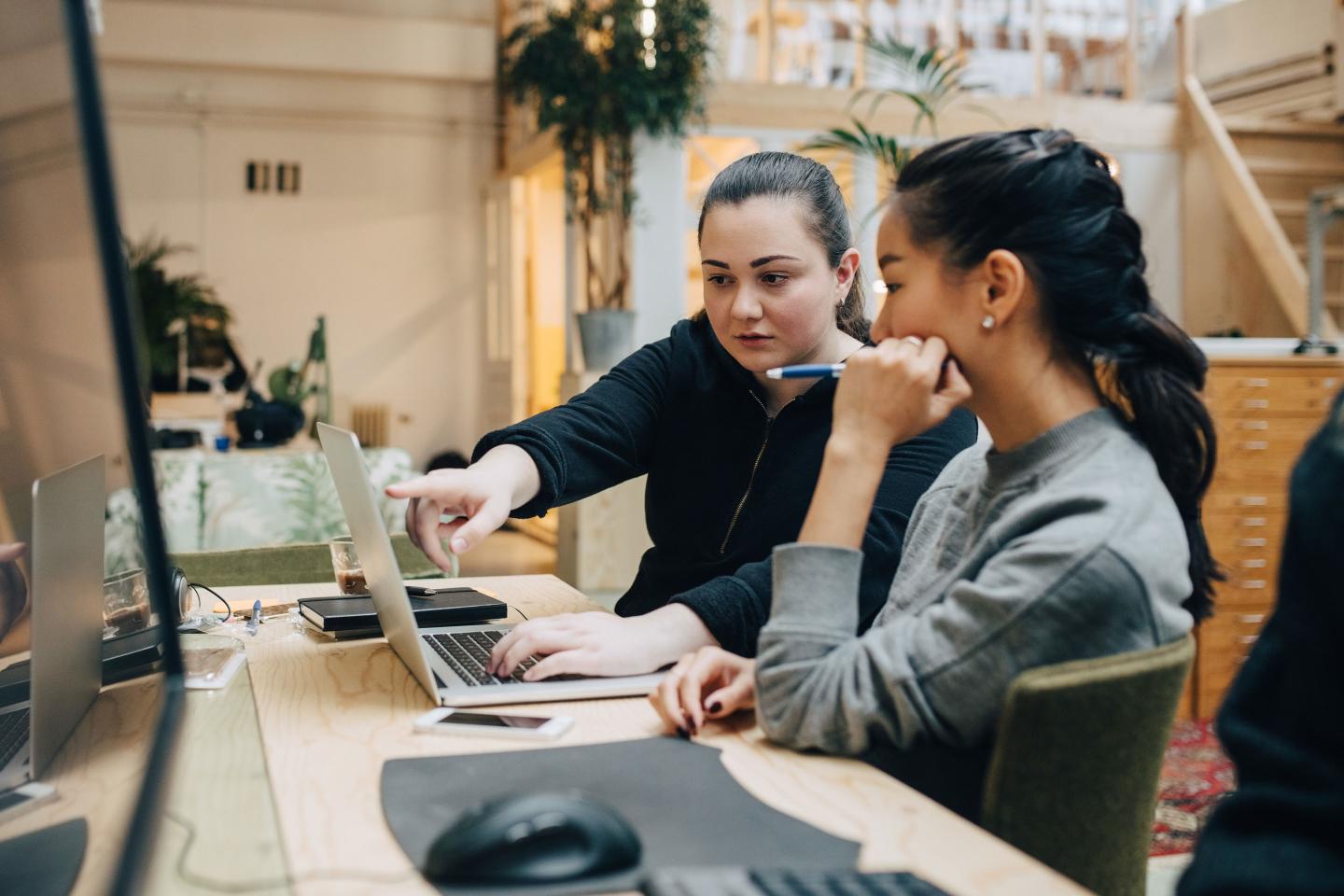 Female coworkers discussing coding on laptop while sitting in office