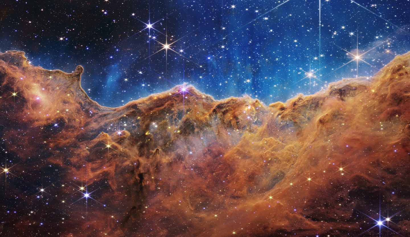This landscape of “mountains” and “valleys” speckled with glittering stars is actually showing the edge of a nearby, young, star-forming region called NGC 3324 in the Carina Nebula. Captured in infrared light by NASA’s new James Webb Space Telescope, this image reveals for the first time previously invisible areas of star birth.