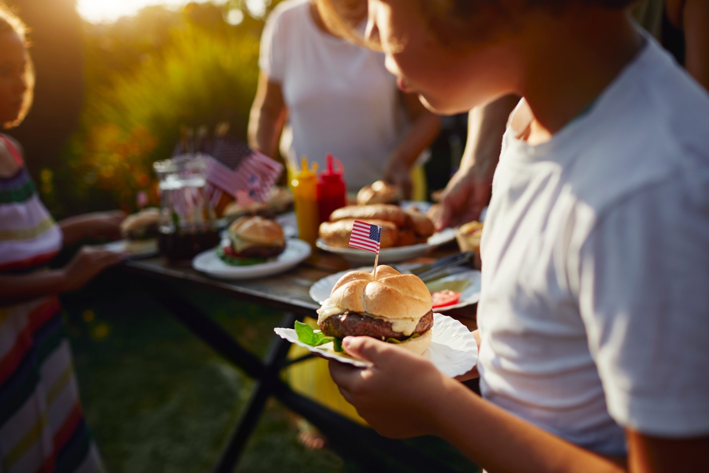 Multi generations on picnic in back yard eating burgers and celebrating 4th of July - Independence Day.
