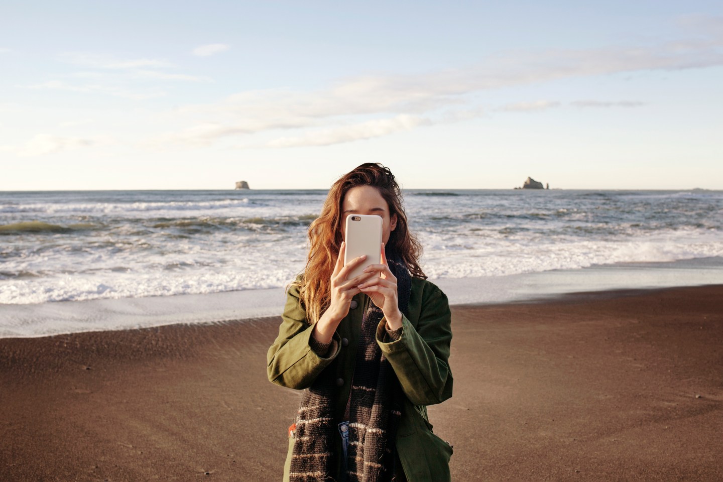 A young woman takes a picture with her phone on the beach.