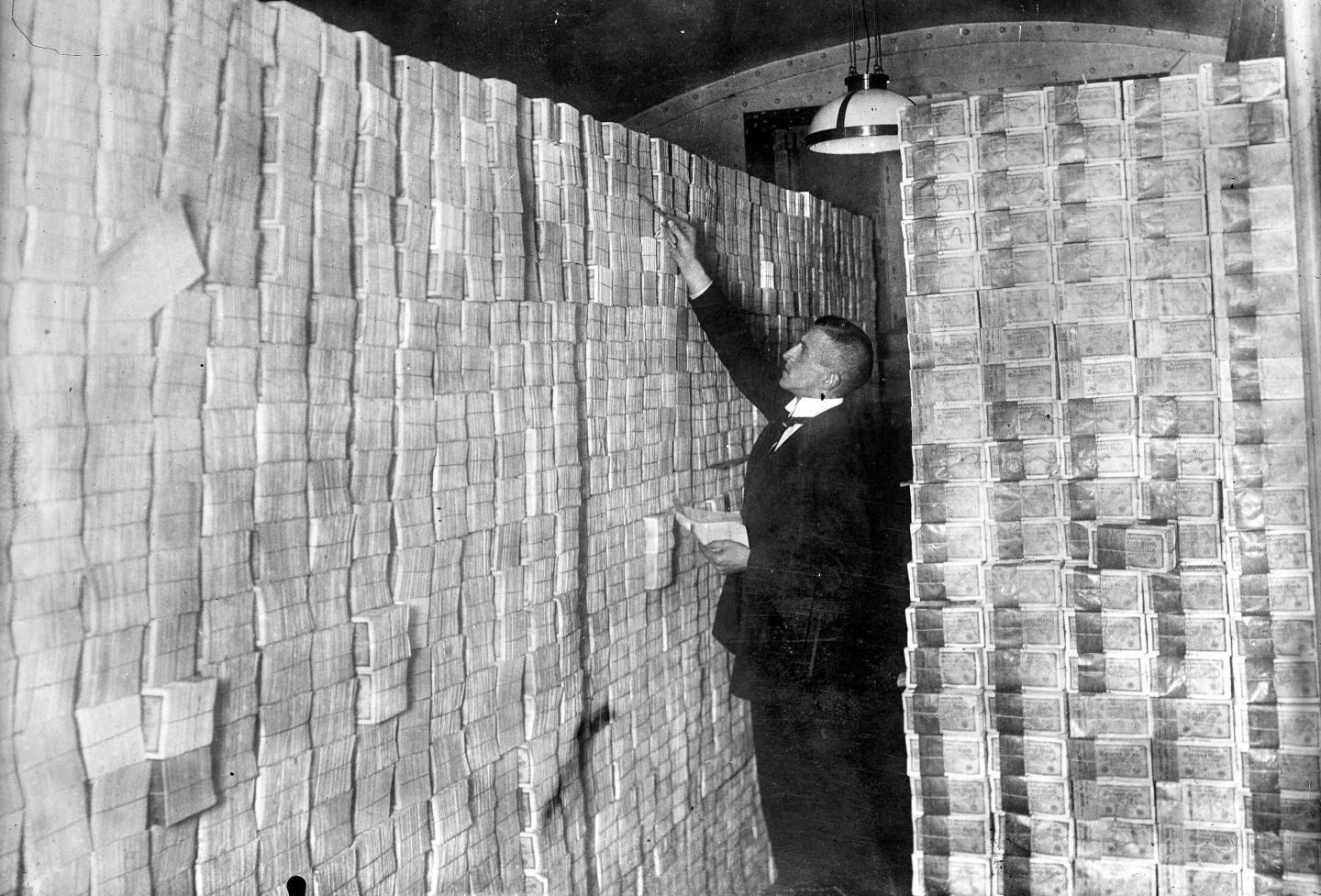 A man stands in front of stacks of banknotes in Germany in 1923.