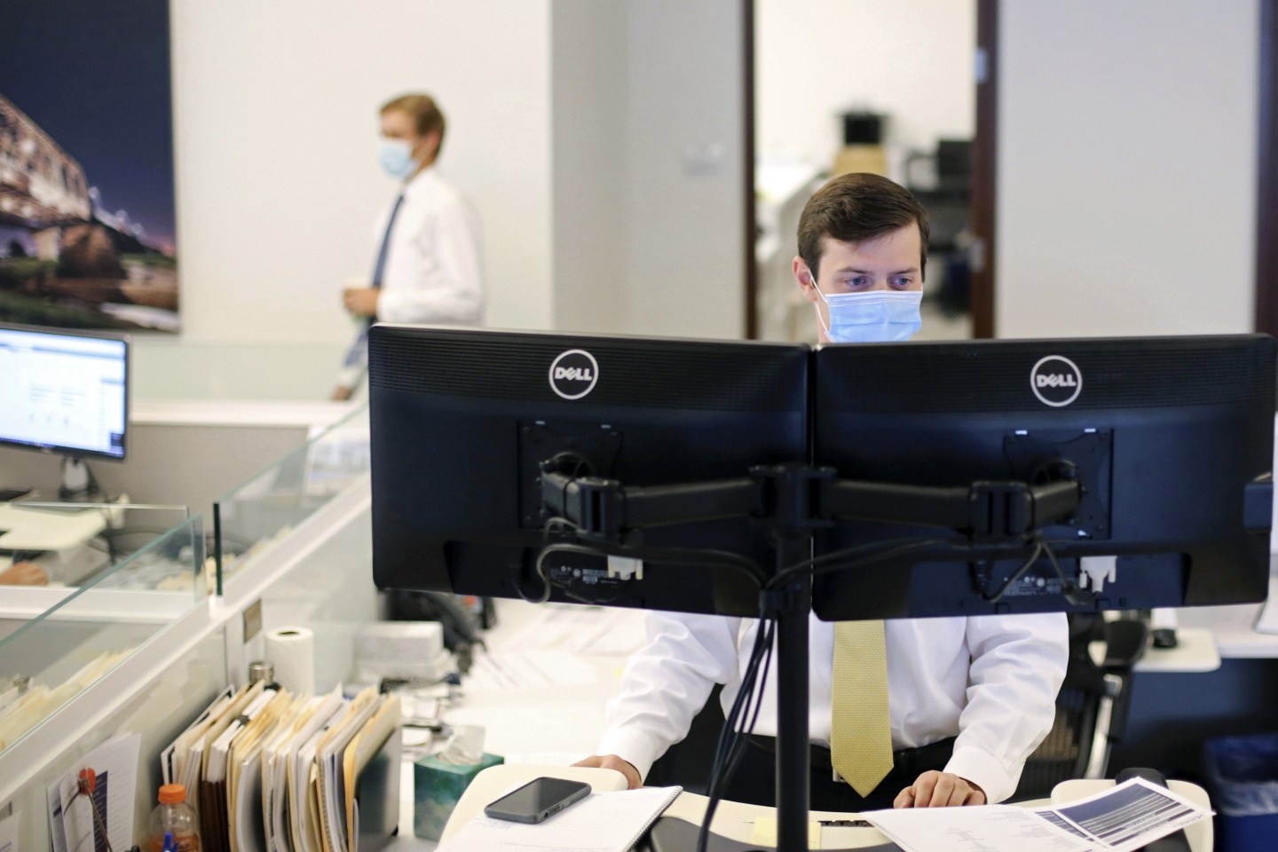 An employee wears a protective mask while working at a computer station at a JLL office in Dallas, Texas.