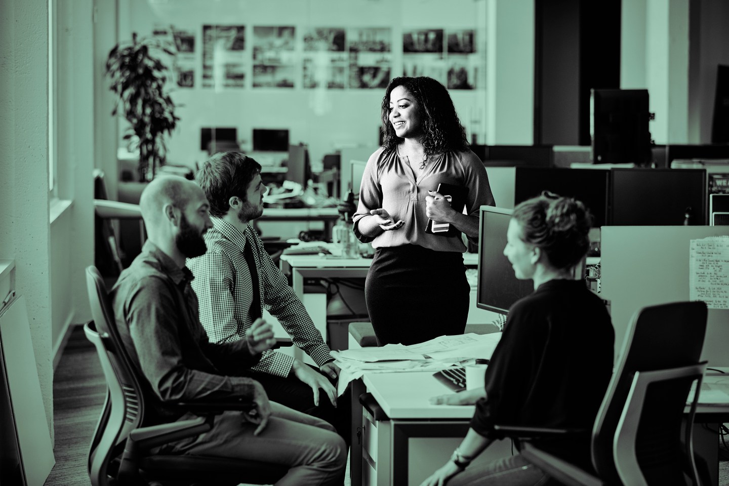 Businesswoman leading informal meeting with colleagues at office workstation.