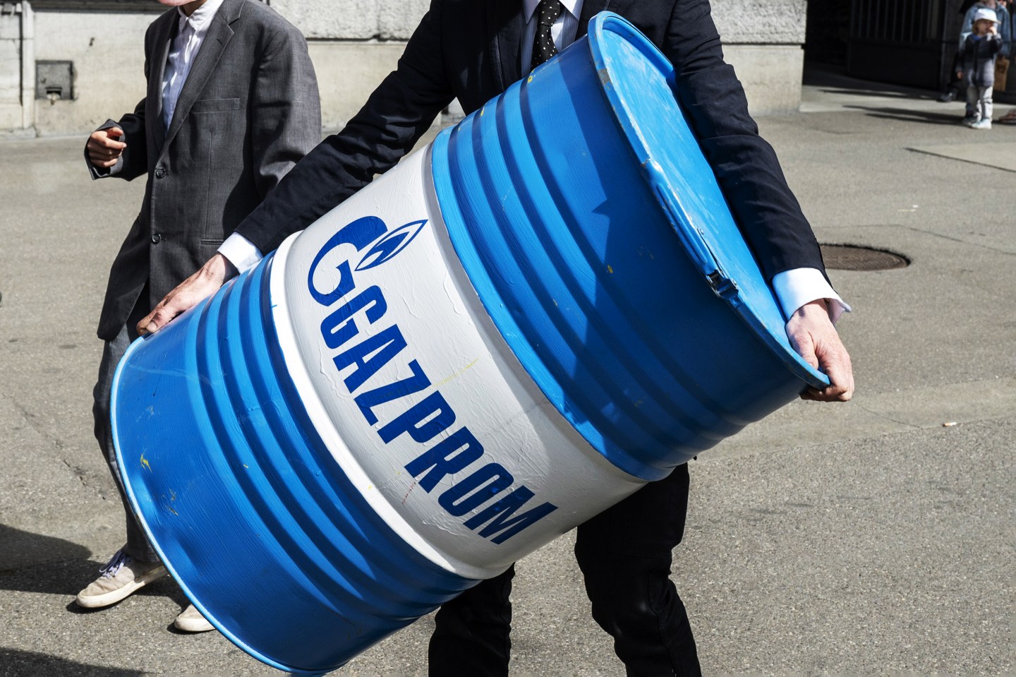 A man in a suit carries branded oil barrel with Gazprom logo.