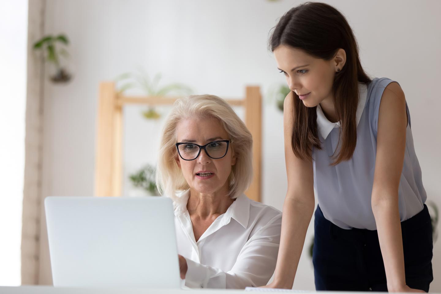 A young woman helps an older woman employee on her computer.