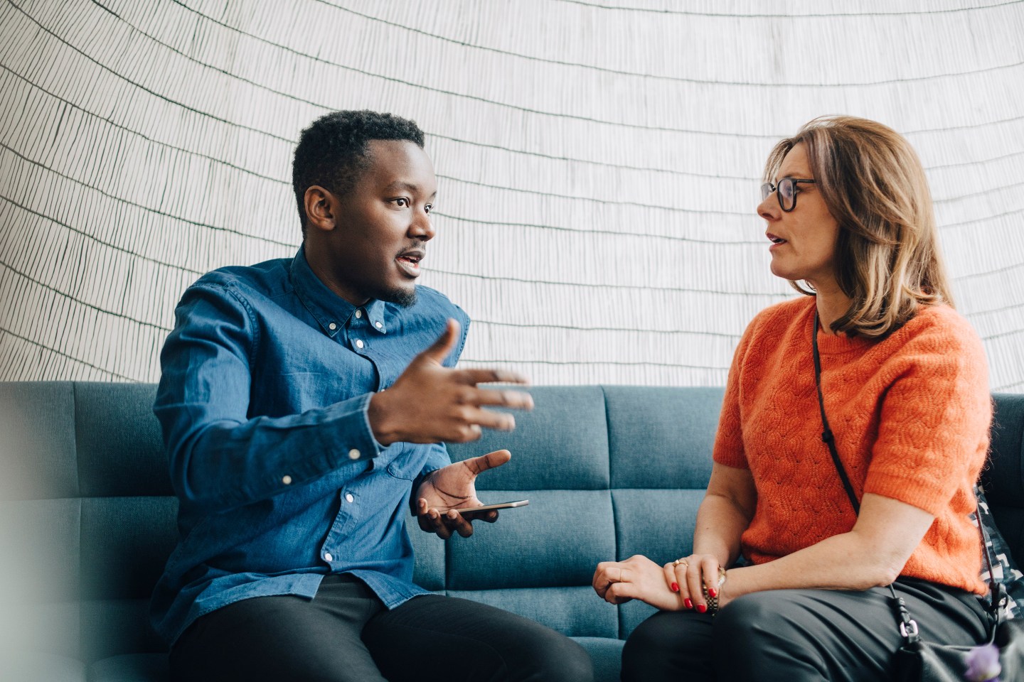 Businessman sharing ideas with female colleague while sitting on couch at conference.