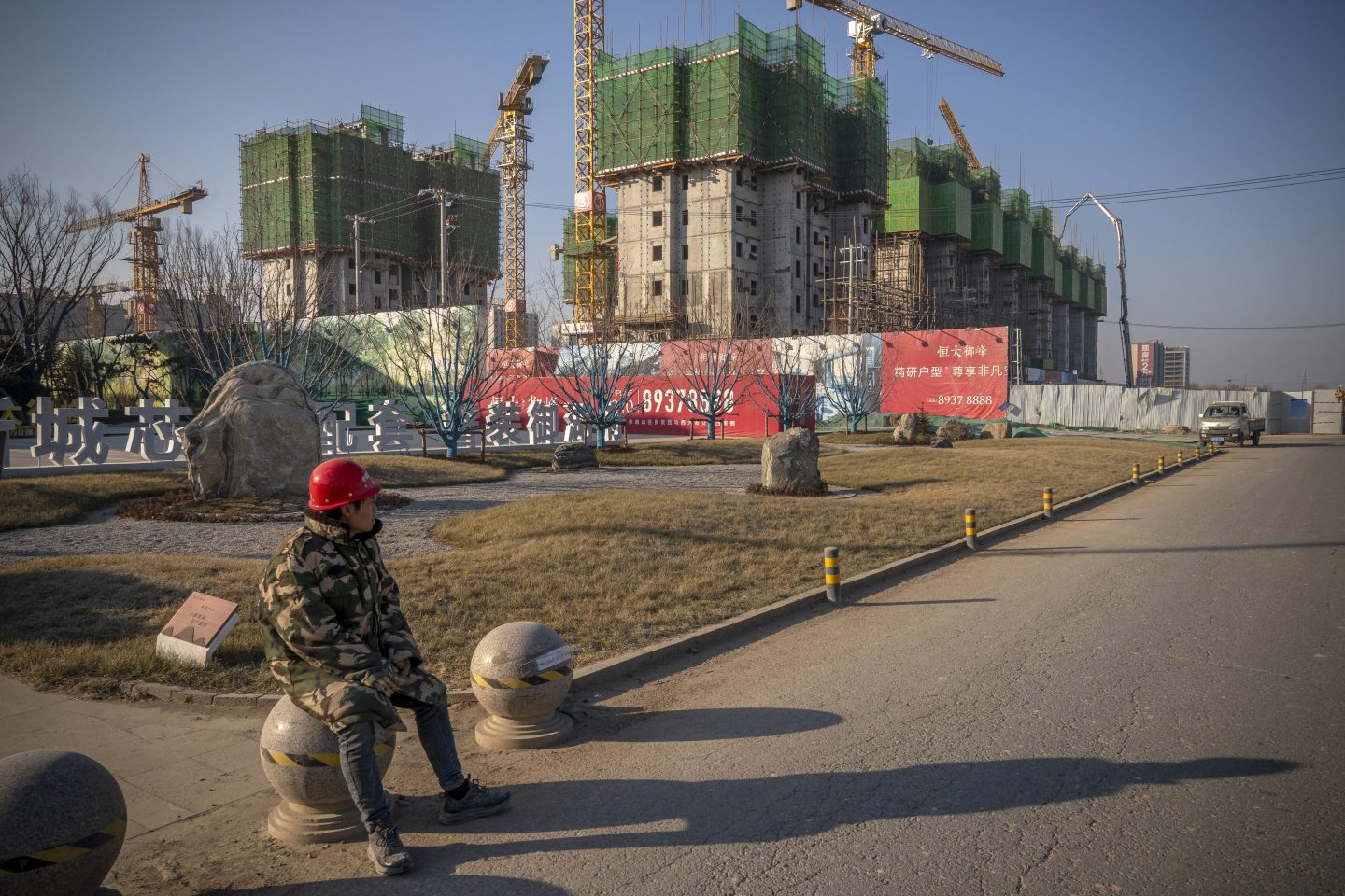 A worker sits in front of the construction site of an unfinished building project by China's Evergrande Group.