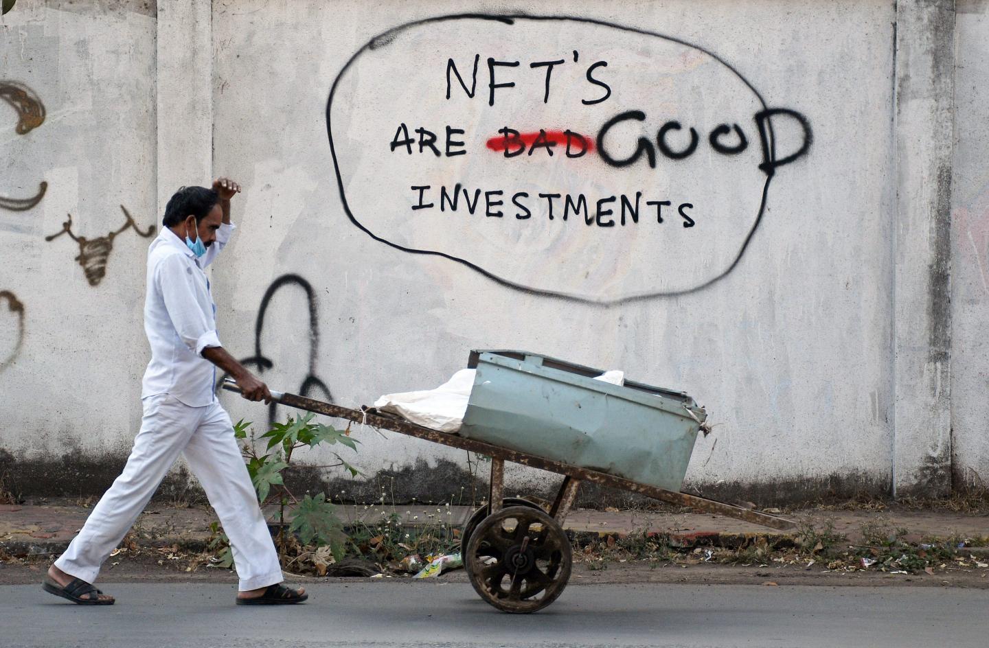 A scrap dealer wearing a protective face mask pushes his handcart past a graffiti painted on a wall that reads "NFT's are good investments" in Mumbai on Feb. 18, 2022.